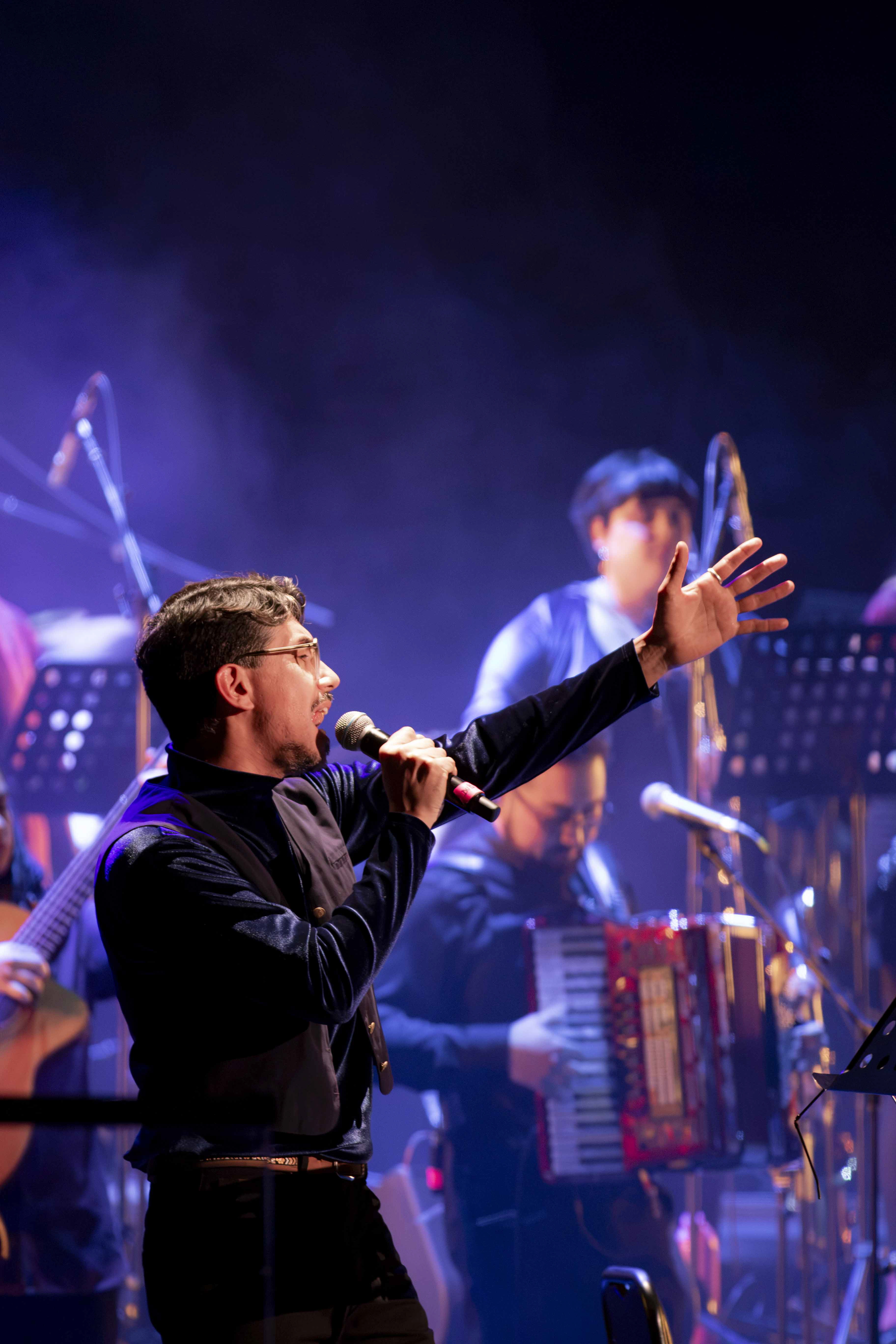 Duberly interpretando en escenario con luz azul y vestuario oscuro.